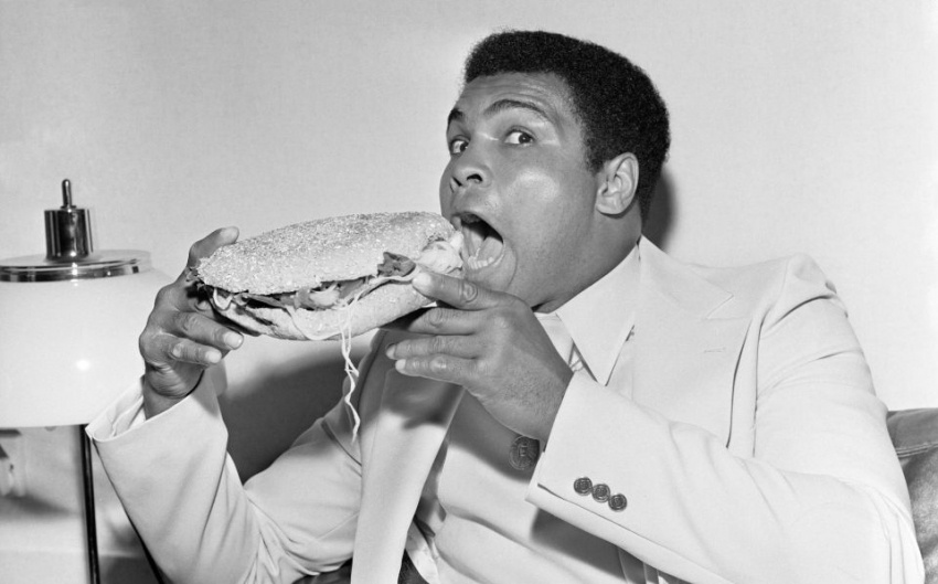 Muhammad Ali a punto de hincar el diente a un bocadillo con lechuga, cebolla y tomate t&iacute;pico del sur de Estados Unidos en 1977.